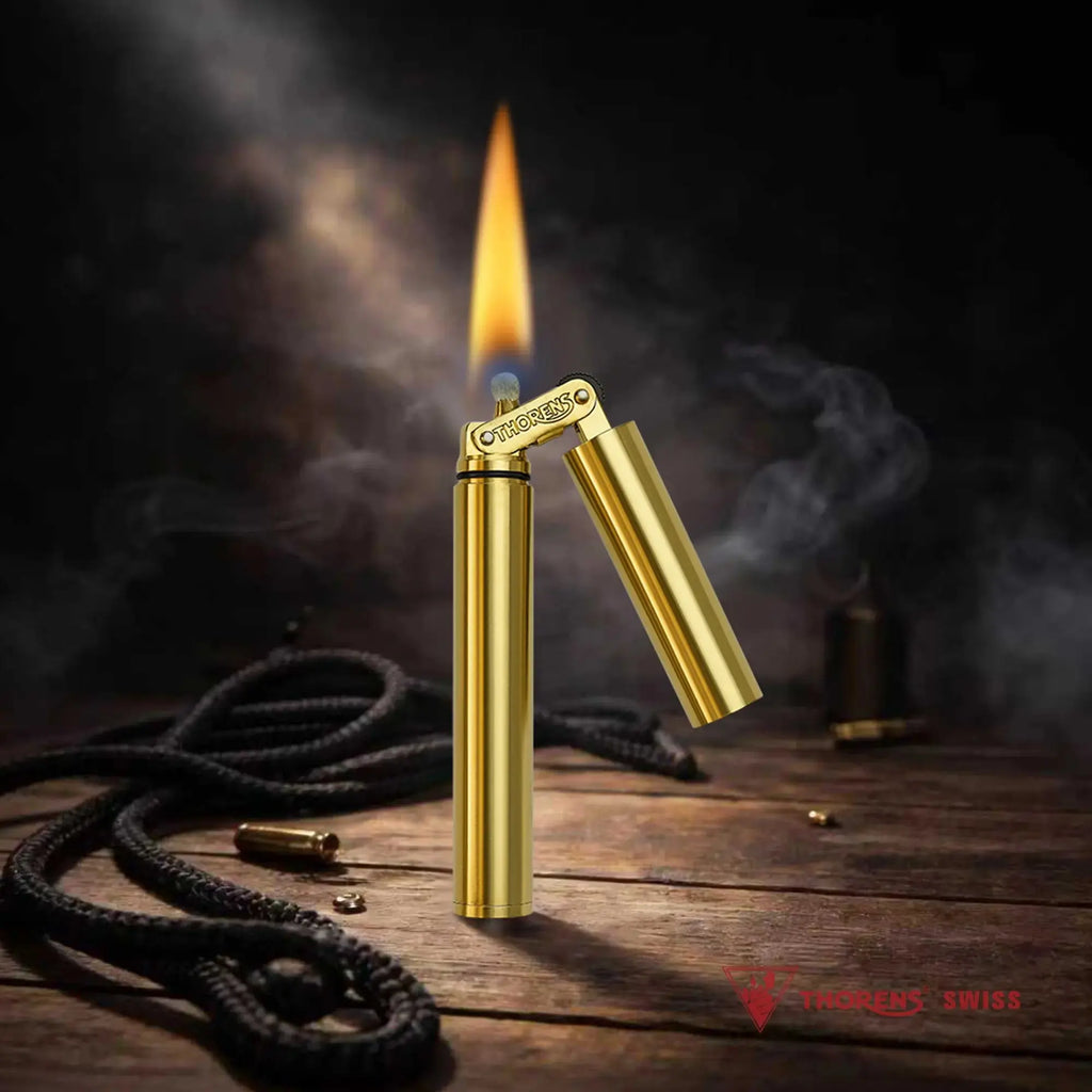 A Thorens Nunchaku lighter in a vibrant gold finish standing ignited on a rustic wooden surface, featuring a steady yellow flame and atmospheric smoke against a dark workshop backdrop.