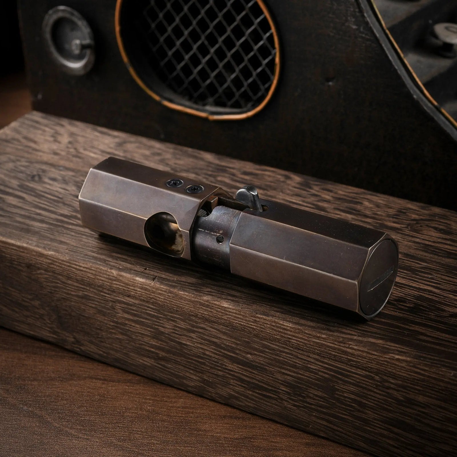 A horizontal perspective of the closed Thorens Octagon Trigger Glossy lighter in antiqued brass, resting on dark wood against a vintage mechanical background.