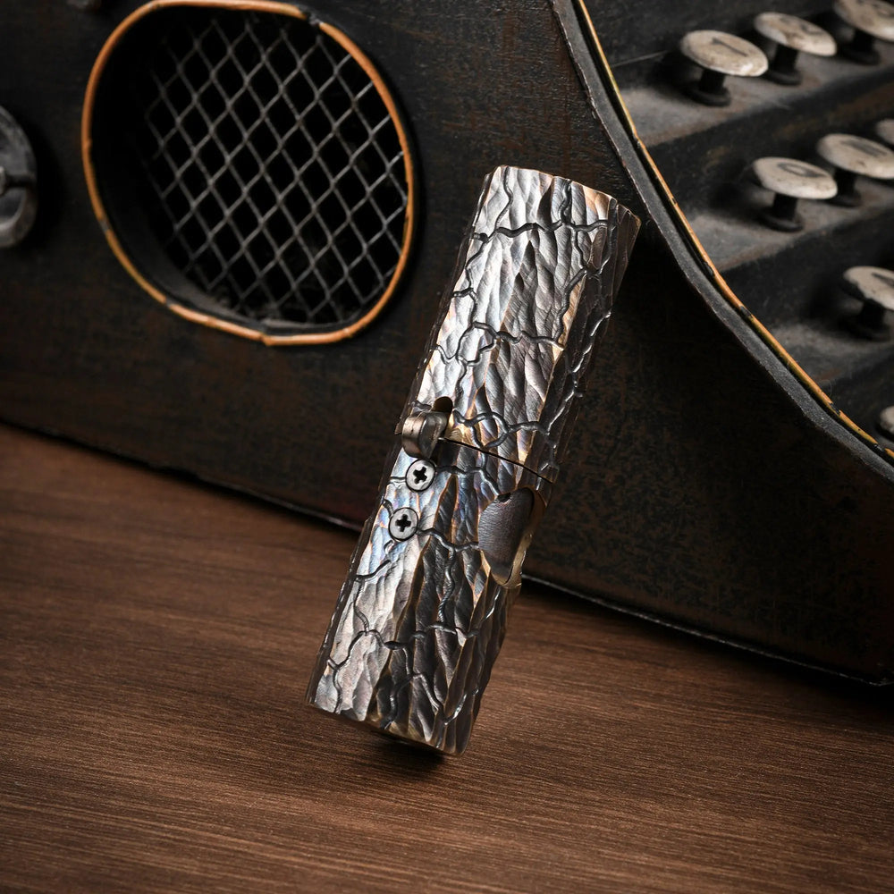 Vertical shot of an Octagon Trigger lighter showing the hand-carved earth fissure texture on antiqued brass against a vintage background.