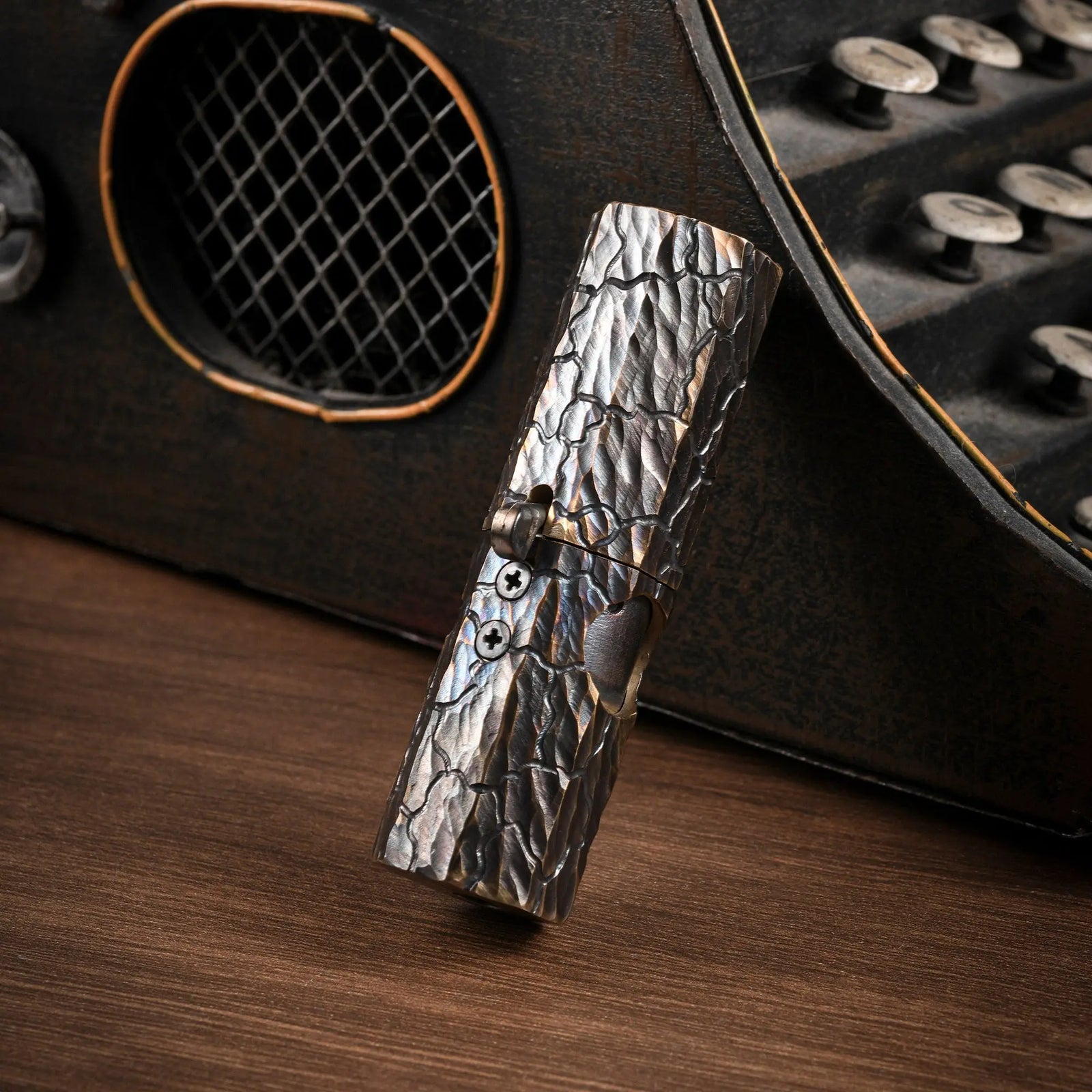 Vertical shot of an Octagon Trigger lighter showing the hand-carved earth fissure texture on antiqued brass against a vintage background.