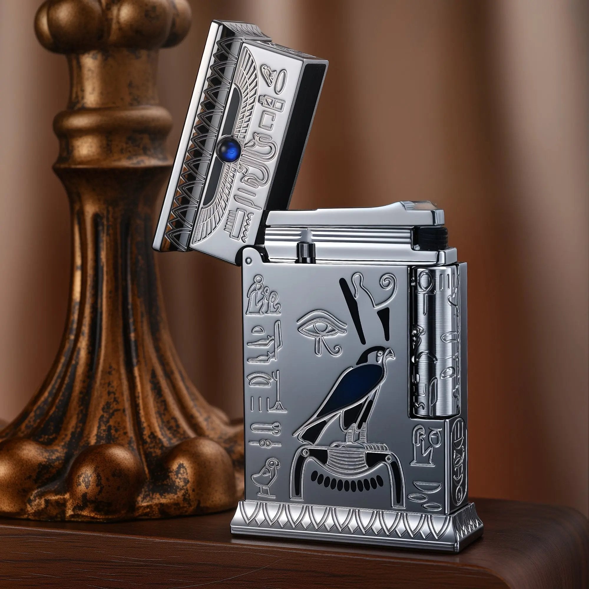 Open-lid silver Thorens lighter with an antique chrome finish, featuring an engraved Horus falcon, Egyptian hieroglyphs, and a blue gemstone.