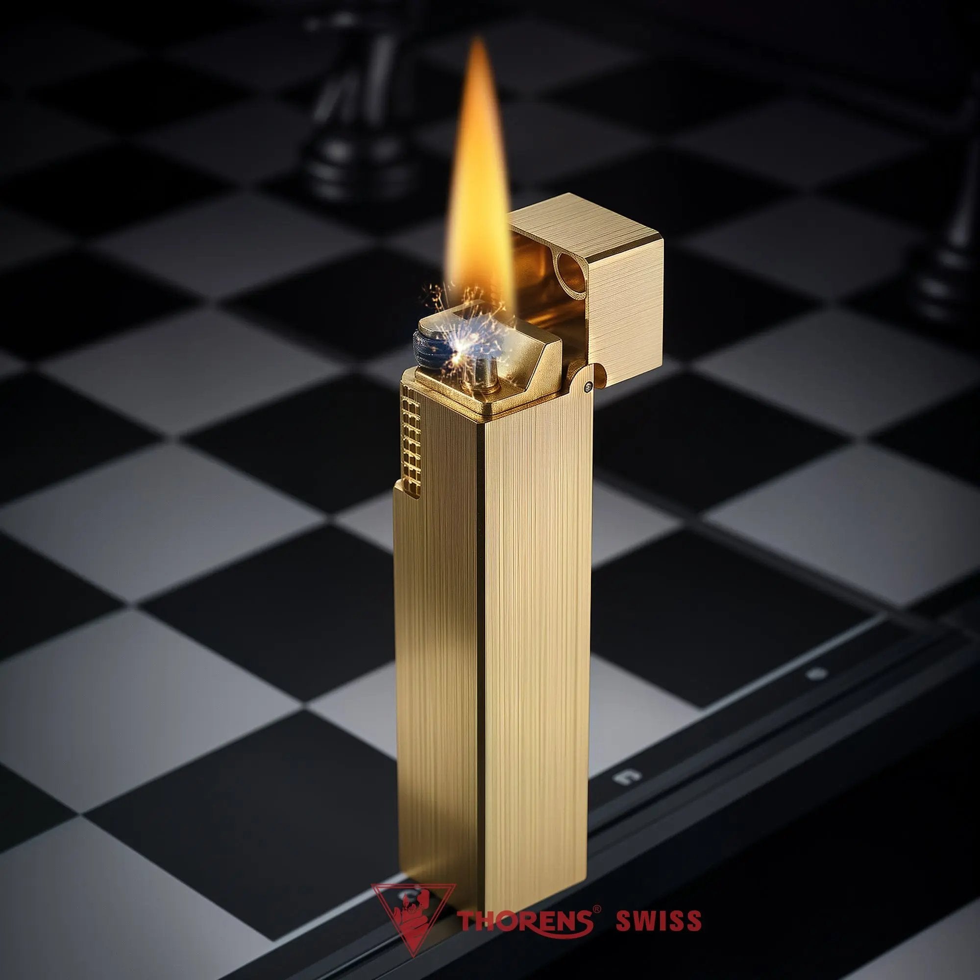 Glossy brass Thorens rectangular side-slip lighter standing upright with the lid open and flame lit, shown on a black and white checkered surface with the ignition wheel and wick clearly visible