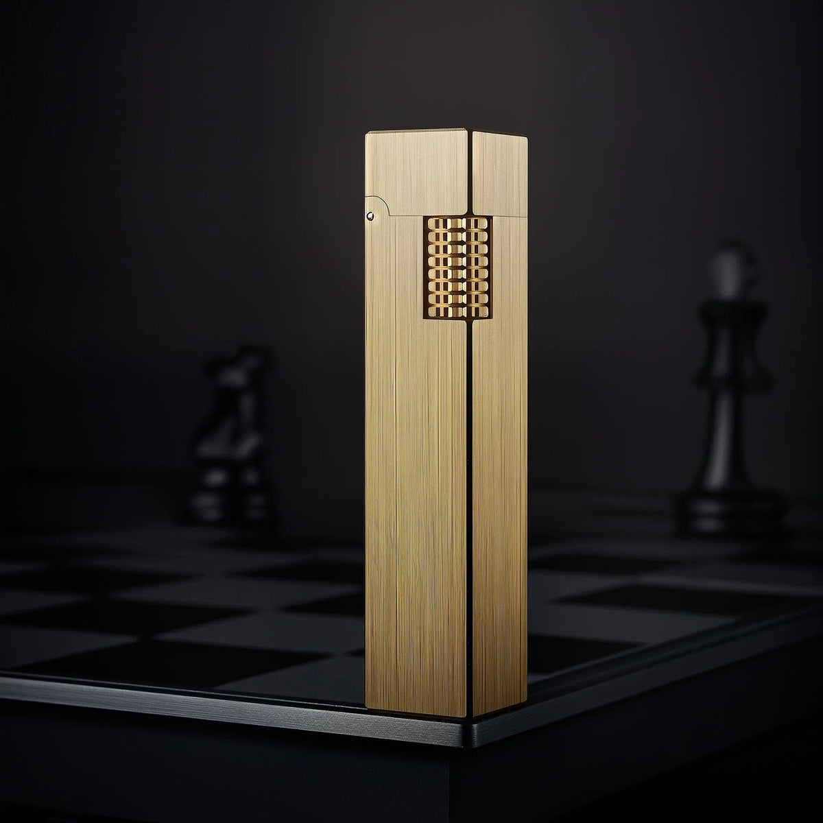 Glossy brass Thorens rectangular side-slip lighter standing upright in the closed position, featuring a brushed linear finish and exposed side ignition wheel against a dark checkered background
