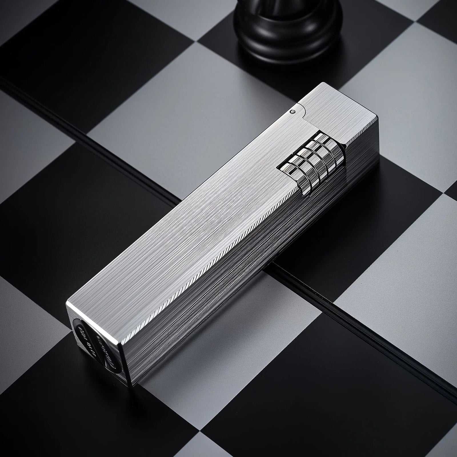 Glossy silver Thorens rectangular side-slip lighter shown in an angled closed view, featuring a linear brushed finish and exposed side ignition wheel on a black and white checkered surface