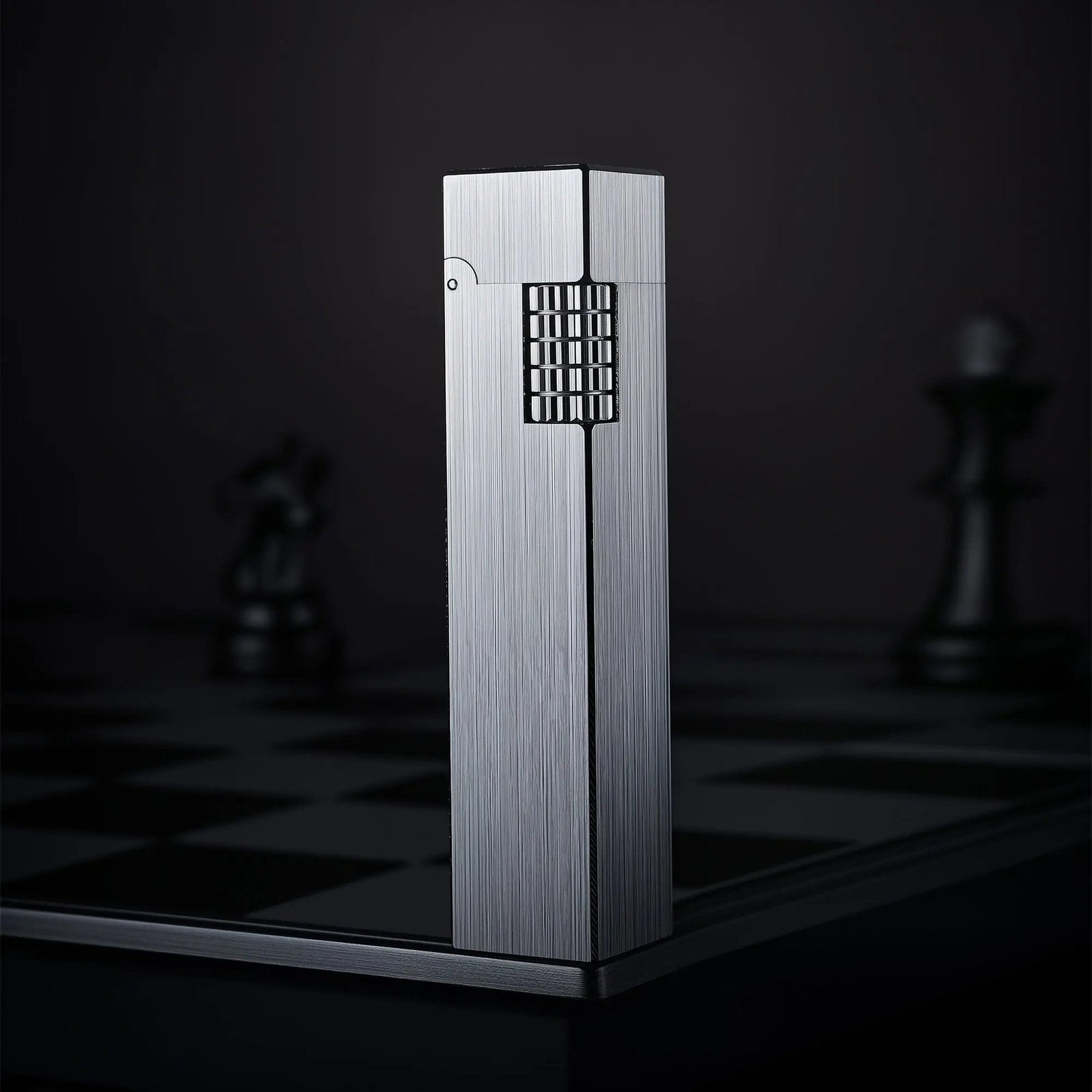 Glossy silver Thorens rectangular side-slip lighter standing upright in the closed position, featuring a brushed linear finish and exposed side ignition wheel against a dark checkered background