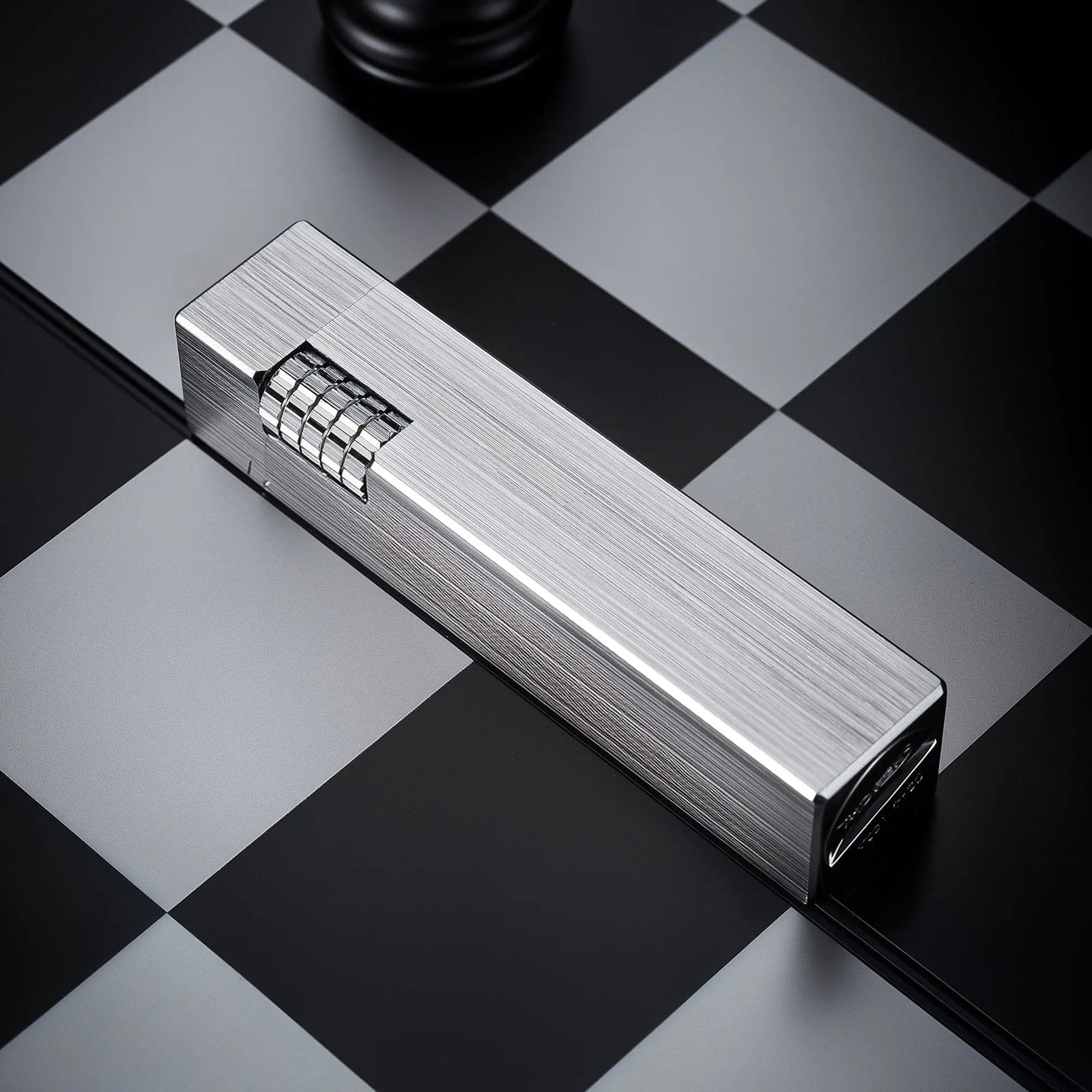 Glossy silver Thorens rectangular side-slip lighter with a linear brushed finish and exposed ignition wheel, placed diagonally on a black and white checkered surface
