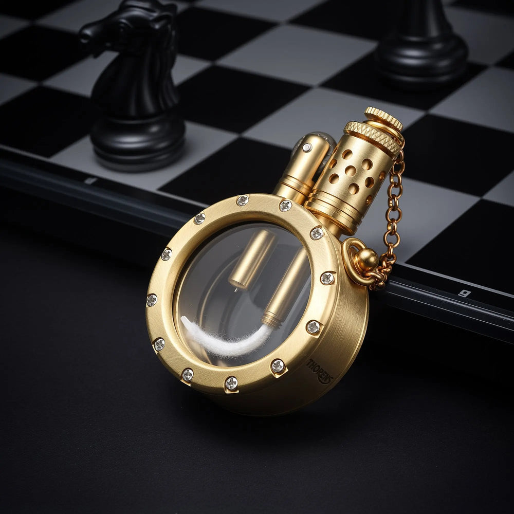A round pocket watch lighter with a transparent fuel chamber and crystal-studded bezel, resting on a chessboard to showcase its mechanical brass craftsmanship.