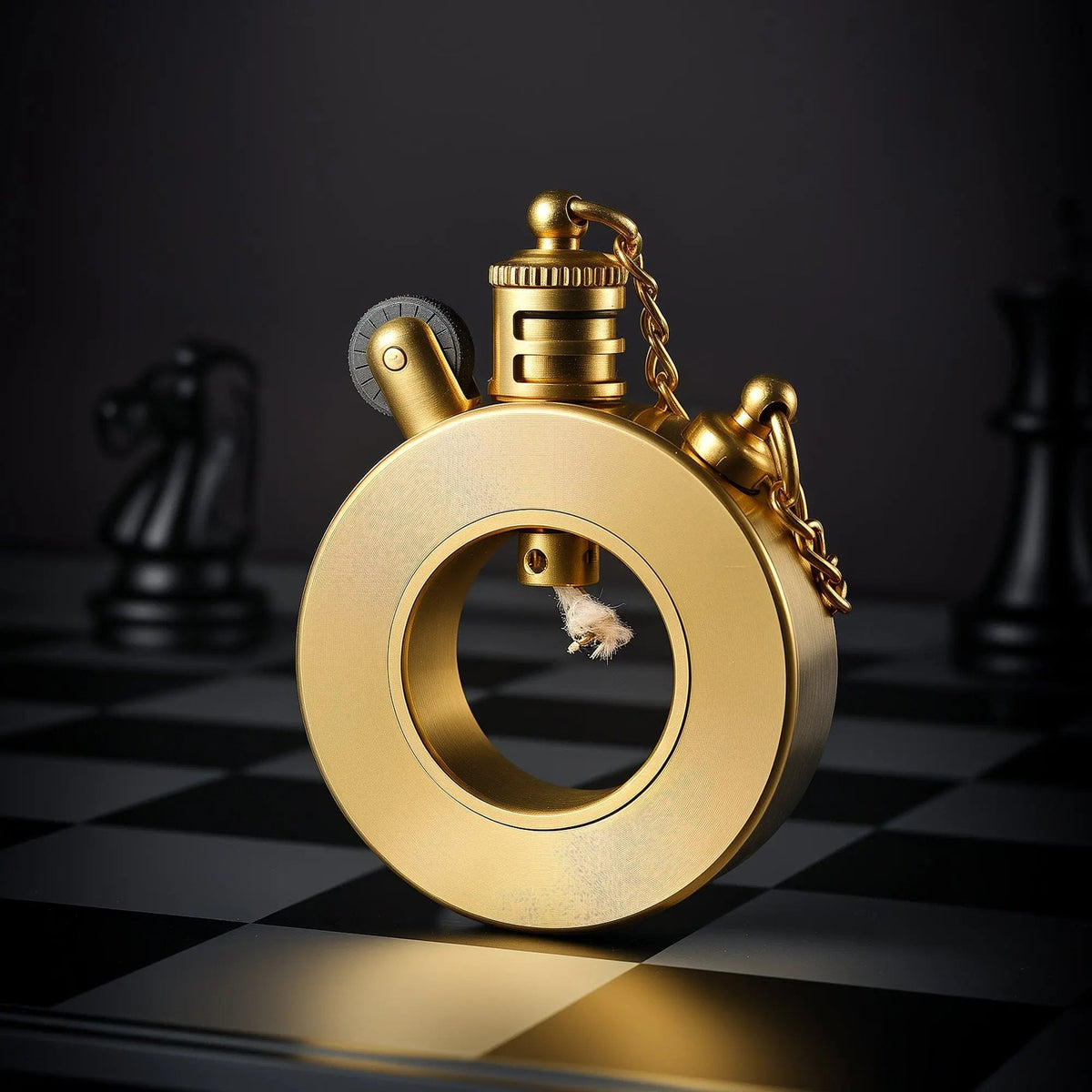 A Thorens Seahorse trench lighter with a circular brass body standing upright on a dark chessboard, showcasing its unique mechanical design and gold-tone safety chain.