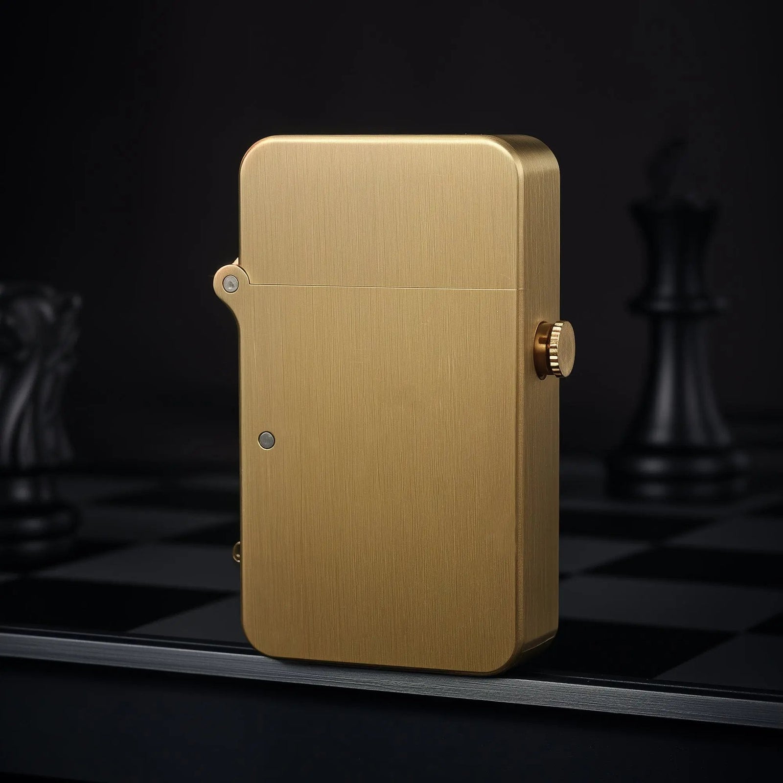 A Thorens semi-automatic ignition lighter in brushed glossy brass stands upright on a dark chessboard, highlighting its sleek profile and precision side button.