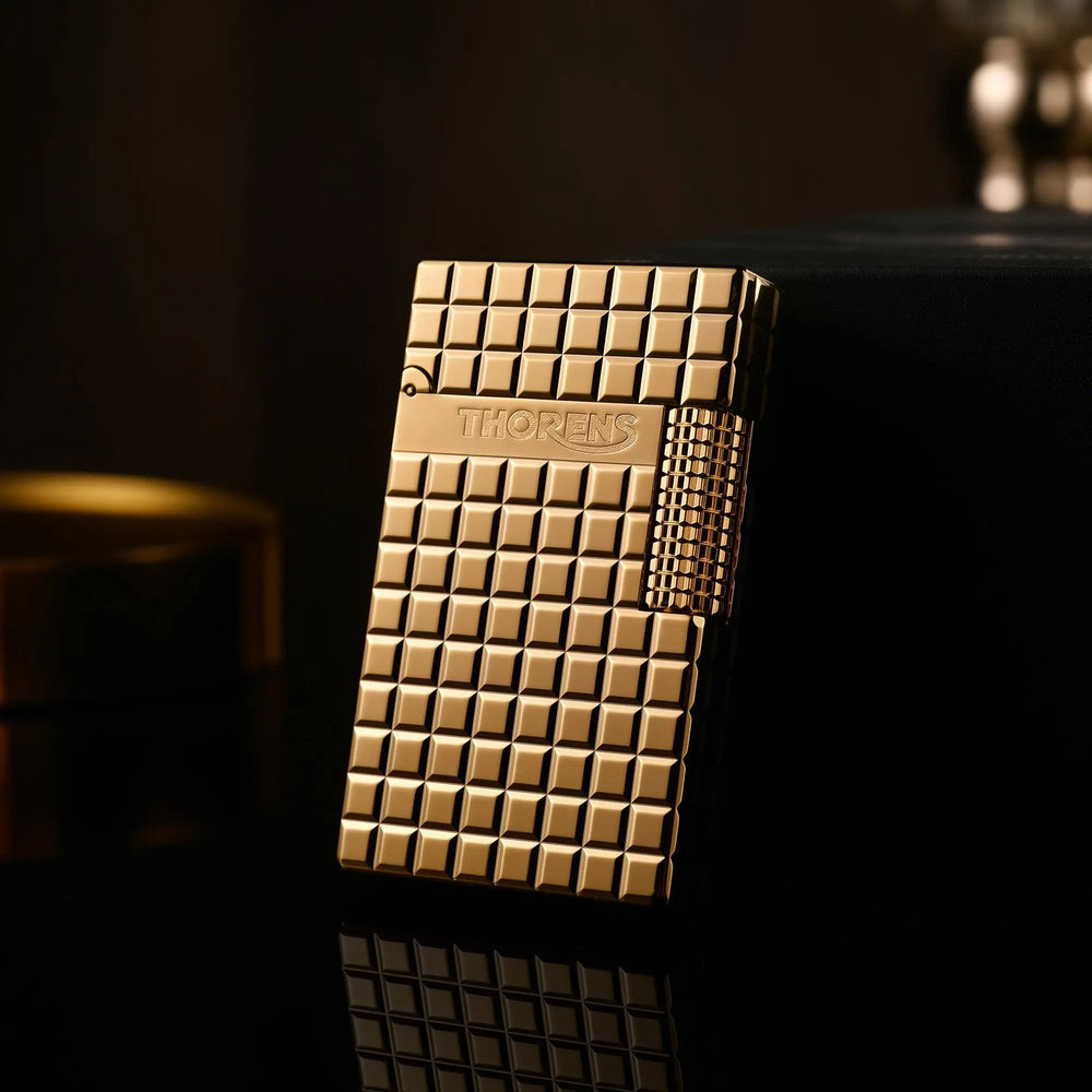 A gold Thorens side slip lighter leaning against a black box, showcasing the high-polish auric block pattern and side-roller ignition.