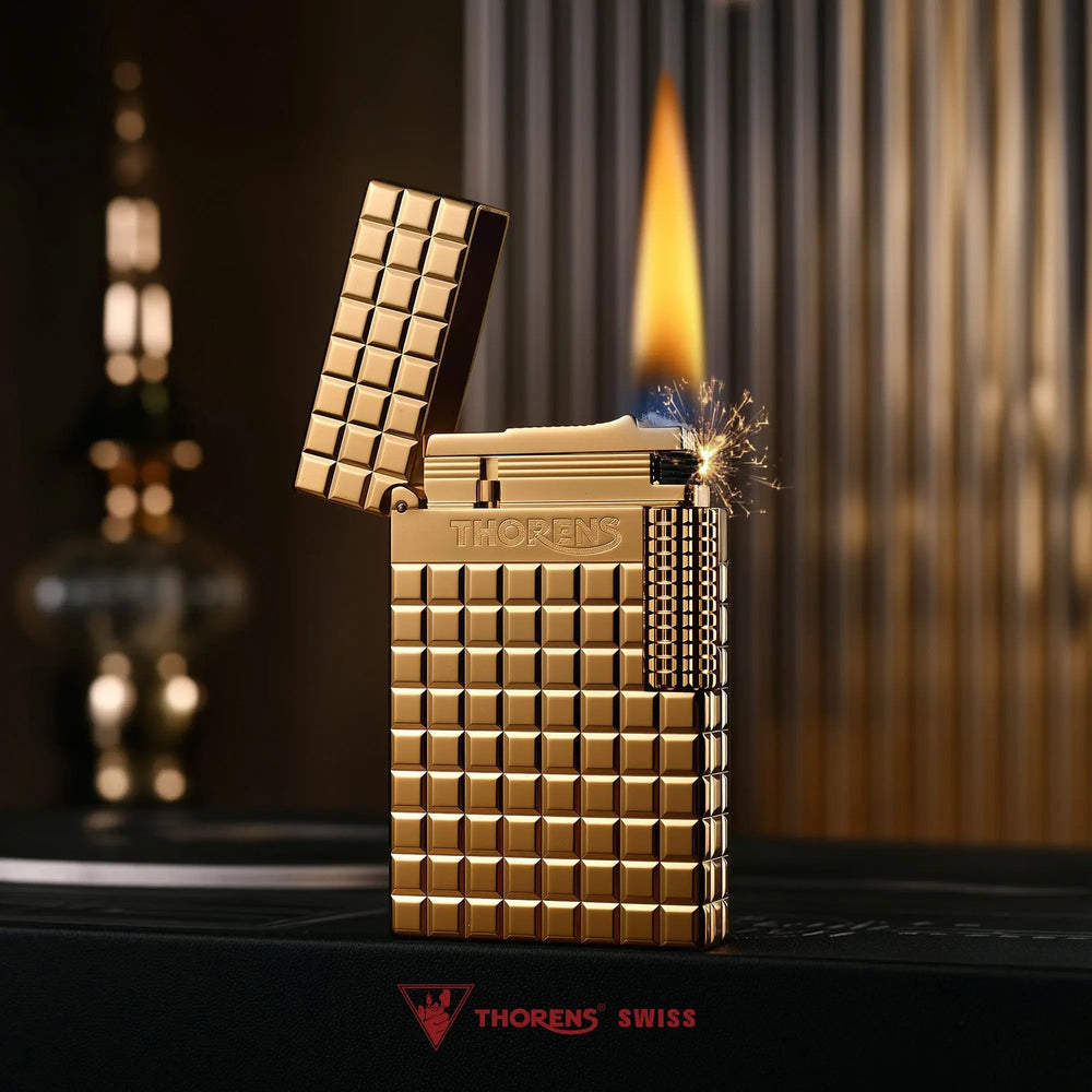 An ignited gold Thorens side slip lighter showing a steady flame and active sparks, highlighting the polished auric block texture and side roller.
