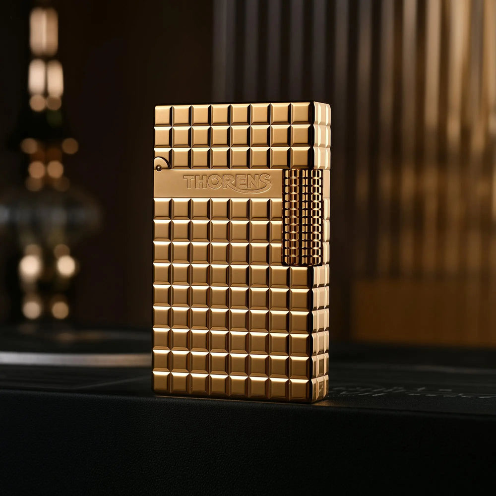A closed gold Thorens side slip lighter featuring a polished auric block pattern, precision side-roller ignition, and engraved brand logo.