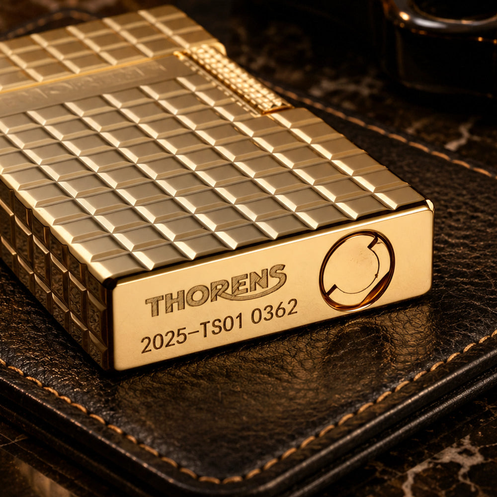 A closed gold Thorens side slip lighter featuring a polished auric block pattern, precision side-roller ignition, and engraved brand logo.