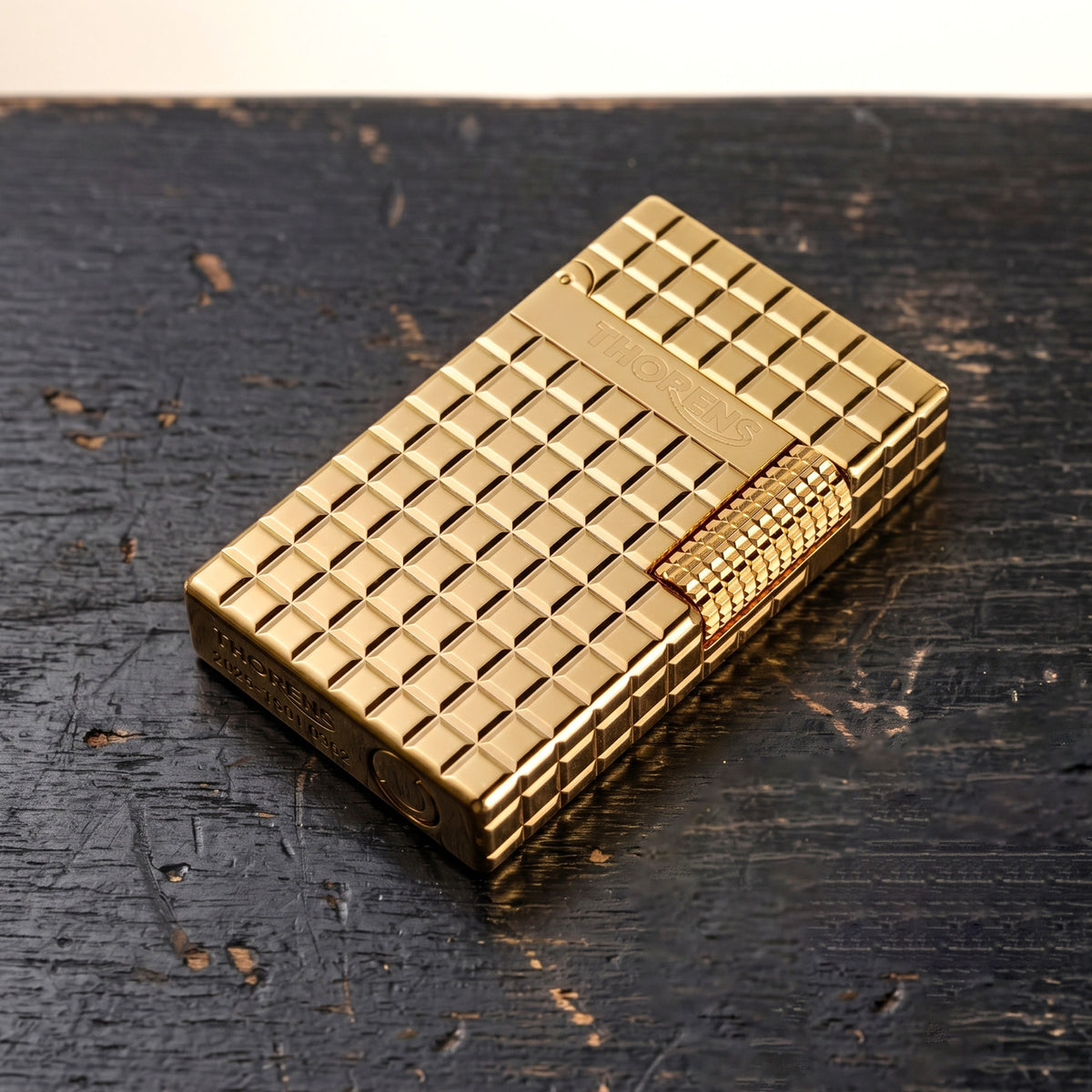 A closed gold Thorens side slip lighter featuring a polished auric block pattern, precision side-roller ignition, and engraved brand logo.