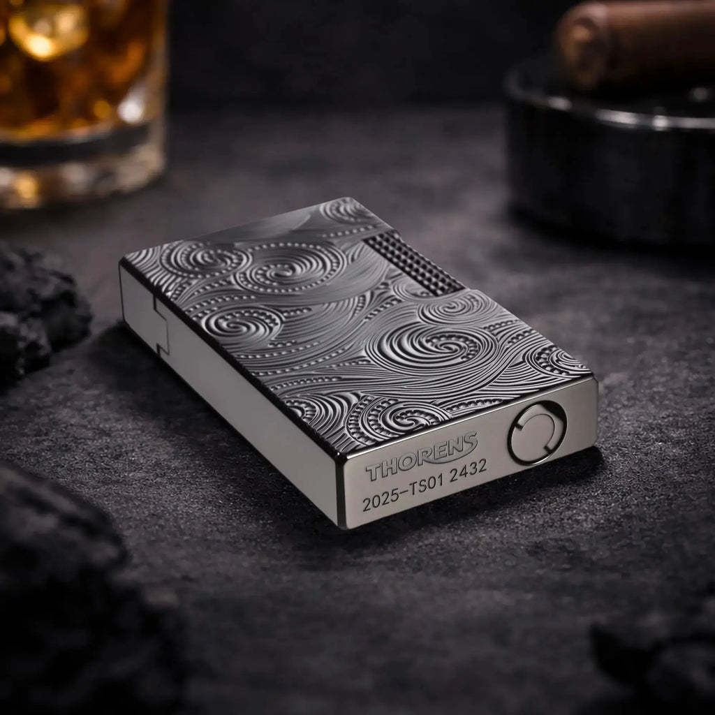 A close-up perspective of the Thorens Side Slip lighter in black with a Vortex engraved pattern, resting on a dark stone surface. The shot highlights the precision-engraved "THORENS" logo and model serial number on the base, emphasizing its mechanical precision and collectible quality.