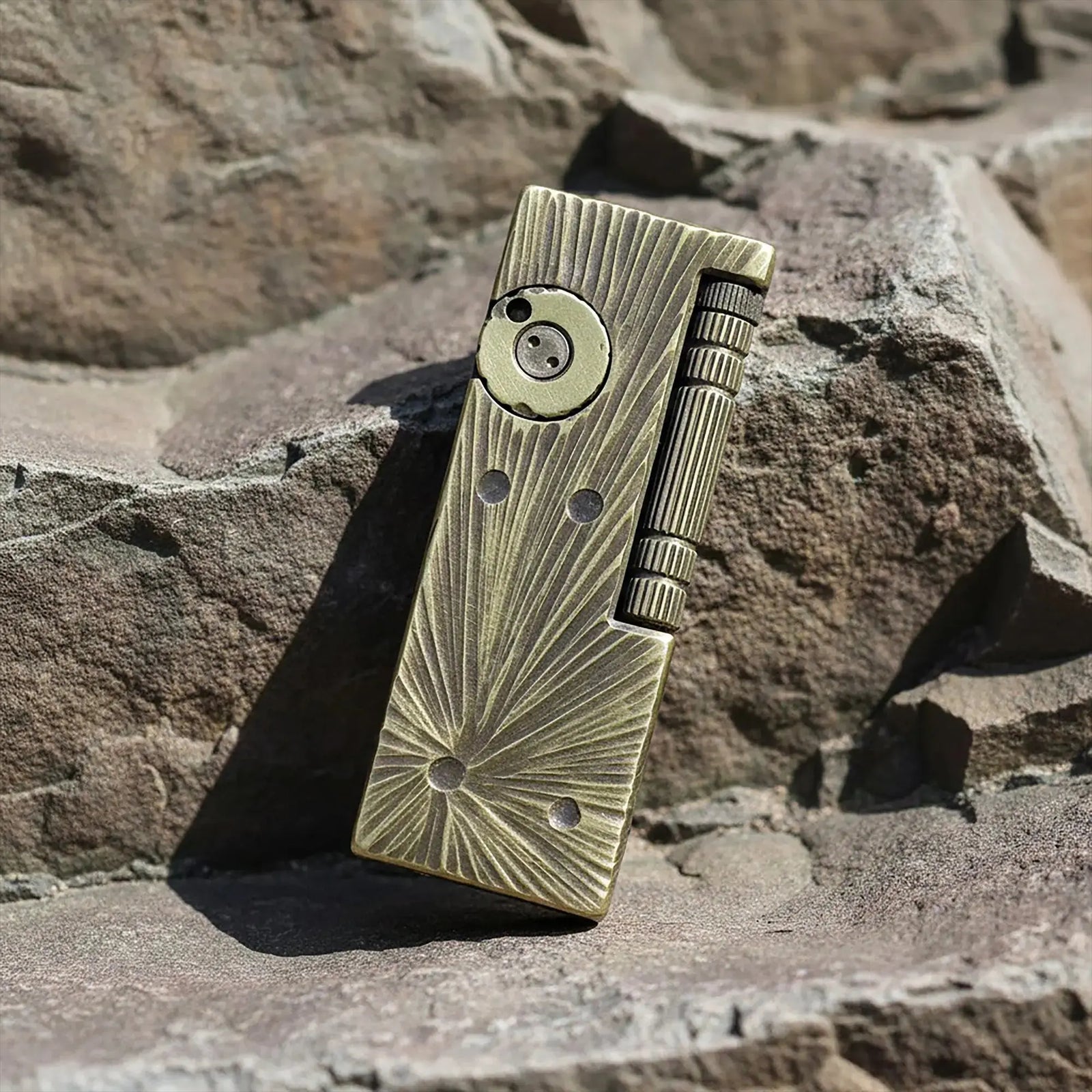 A Thorens Side Slip lighter with the Meteorite Crater textured finish resting on a rugged stone surface, showcasing its antique brass patina and mechanical precision for outdoor EDC.