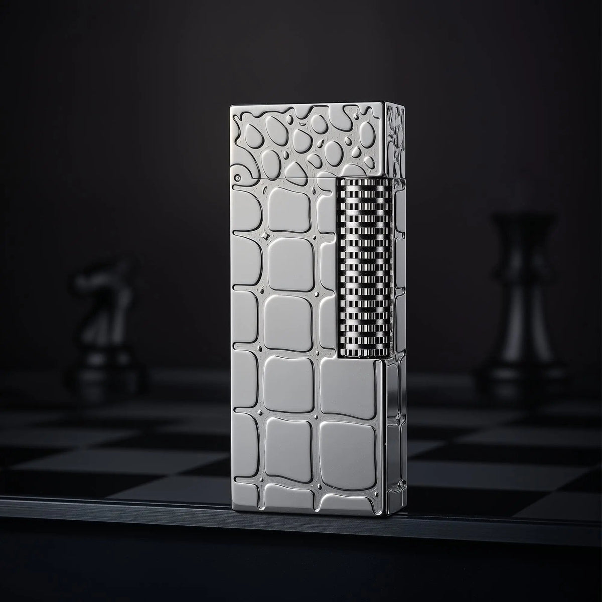 A narrow Thorens side slip lighter with a polished silver crocodile pattern standing upright on a dark chessboard, showcasing its slim profile and refined texture.