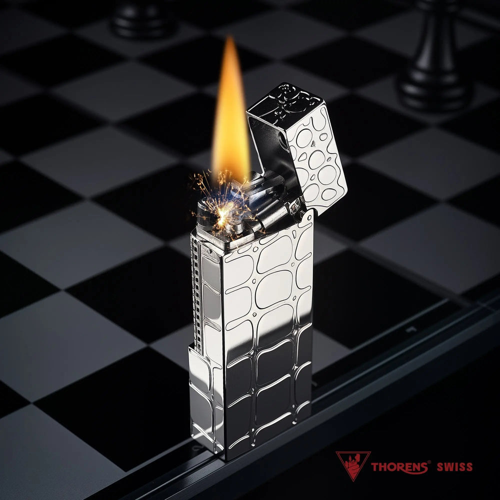 A narrow Thorens side slip lighter with a polished silver crocodile pattern standing on a chessboard, producing a steady flame and sparks.
