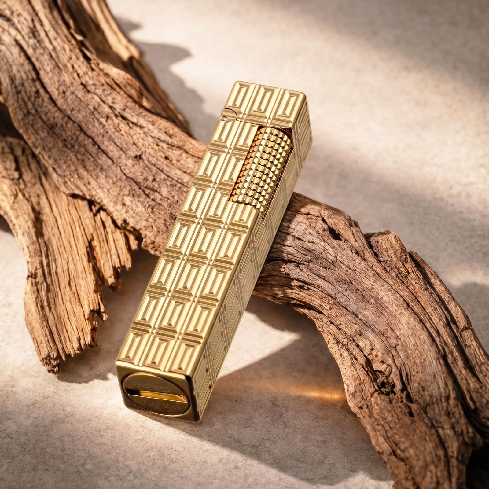 Thorens Side Slip rectangular lighter with geometric block pattern and extended roller in gold finish, displayed closed on driftwood, highlighting the engraved texture and polished metal body.