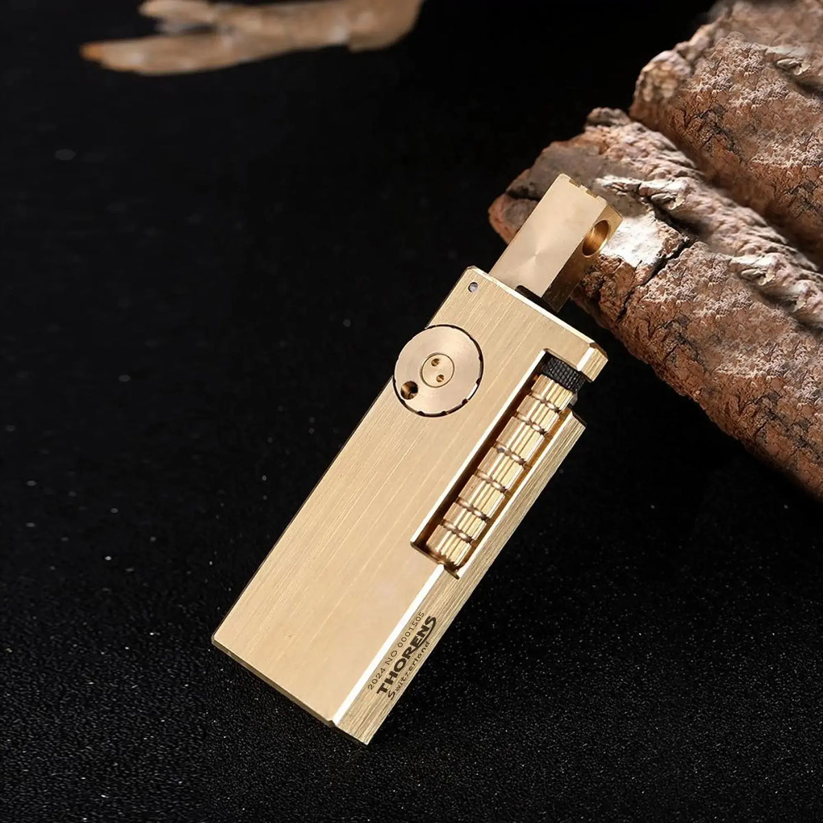A high-angle shot of the Thorens Side Slip lighter in glossy brass resting on a dark textured surface, featuring the iconic open lid and "fish intestines" textured mechanical flint wheel.