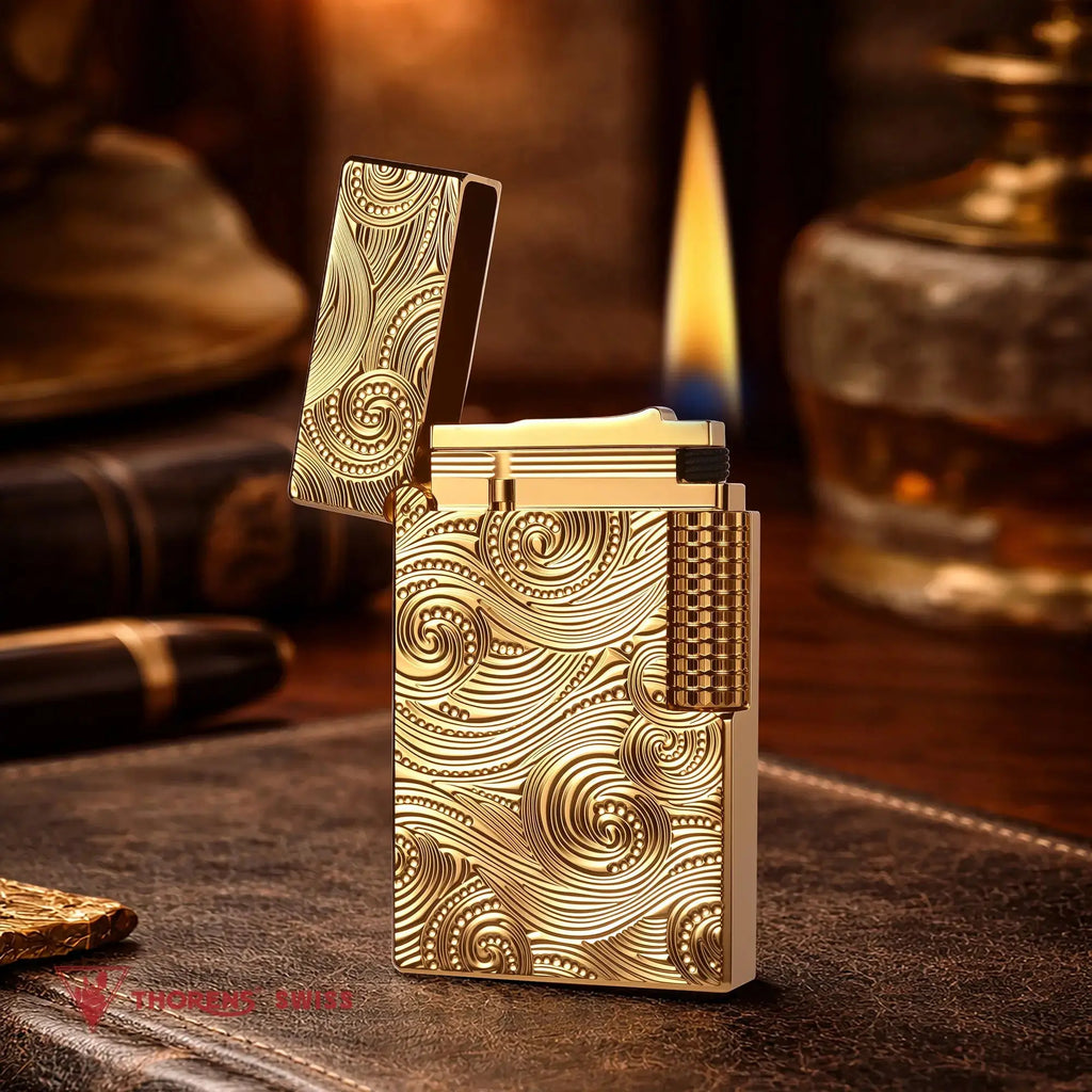 A premium gold Thorens Side Slip lighter with an intricate Vortex engraved pattern, shown standing open with a steady flame against a refined study backdrop, highlighting its heritage brass craftsmanship and collectible aesthetic.