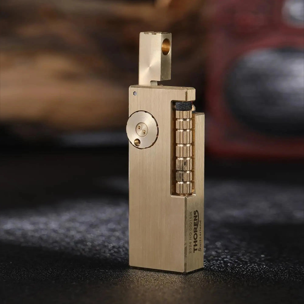 A side profile of the Thorens Side Slip lighter in glossy brass with the lid open, showcasing the mechanical precision of the "fish intestines" vertical flint wheel and the brushed metal finish.