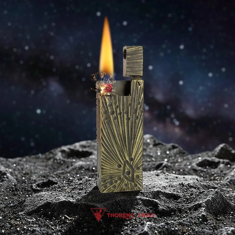 An ignited Thorens Side Slip lighter with the Meteorite Crater antique brass finish, displaying a vibrant flame and mechanical sparks against a celestial lunar backdrop.