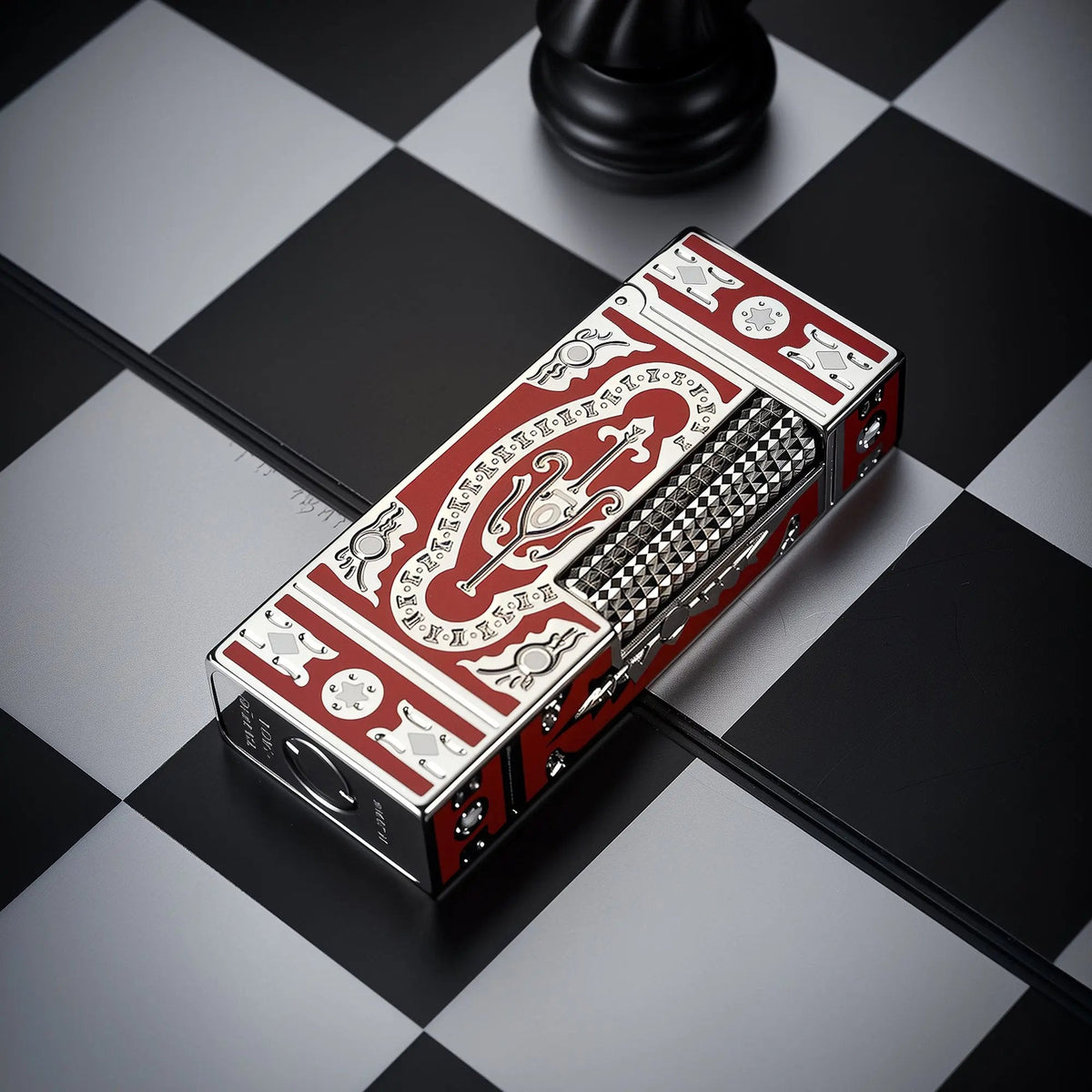 A Thorens Side Slip narrow lighter with a red and silver Holy Grail pattern, resting on a black and white chessboard for a refined collectible aesthetic.