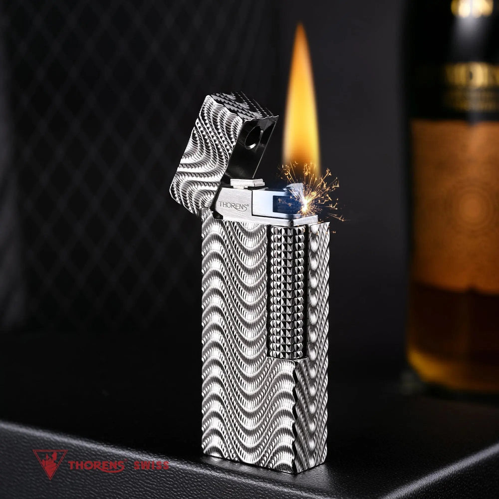 An open Argent Mirage narrow lighter in mid-strike, throwing a burst of sparks and a tall, steady flame that illuminates the high-density silver wave texture against a dark, textured background.