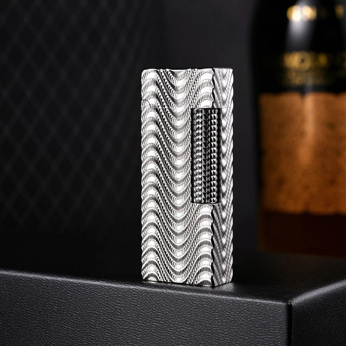 A portrait of the Argent Mirage narrow lighter, highlighting its silver-toned wave texture and diamond-cut ignition roller, set against a dark background with a blurred wine bottle.