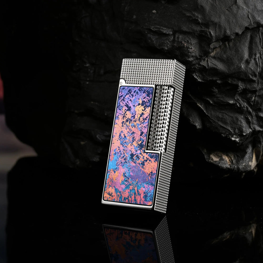 A slim Side Slip lighter featuring an Aurora Violet Ti finish and hobnail texture, leaning against a dark obsidian rock with a sharp reflection.