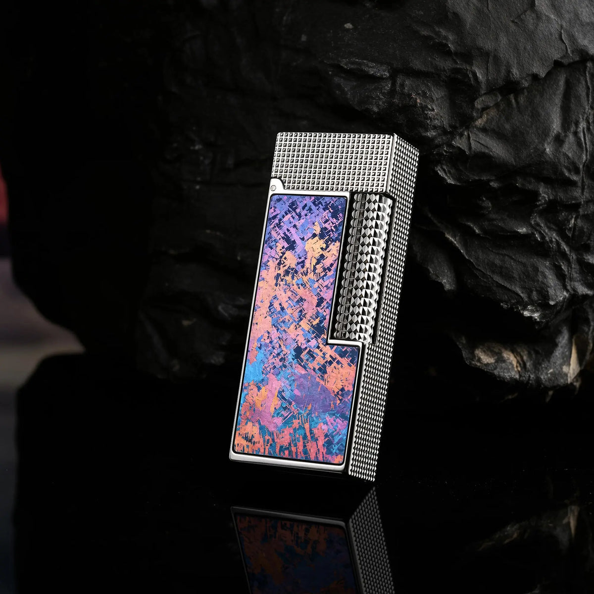 A slim Side Slip lighter featuring an Aurora Violet Ti finish and hobnail texture, leaning against a dark obsidian rock with a sharp reflection.
