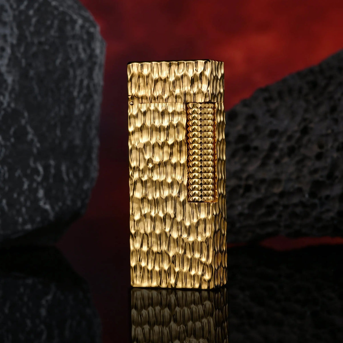 A closed Golden Crater narrow lighter showing a high-gloss hammered gold texture and hobnail ignition roller between two dark volcanic stones.