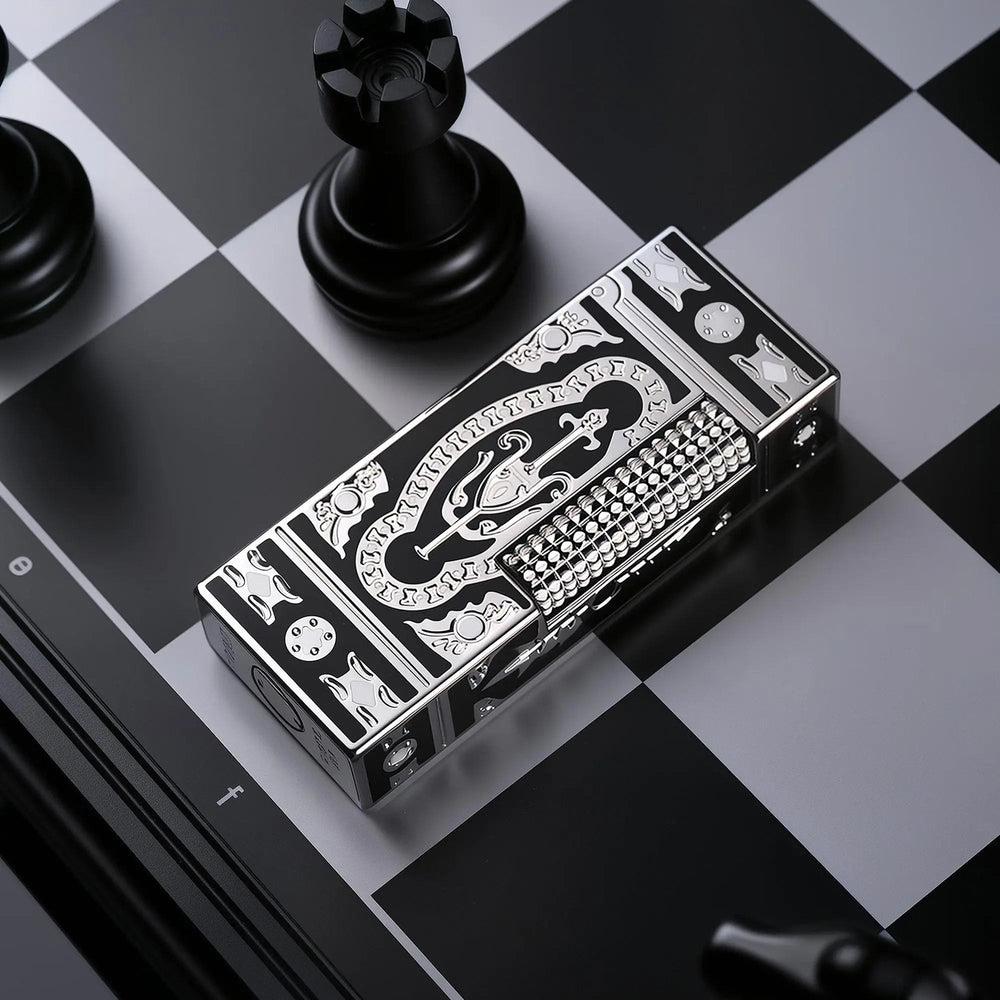A slim Side Slip lighter with a black and silver "Holy Grail" ornate engraved design, resting on a monochrome chessboard next to a black chess rook.