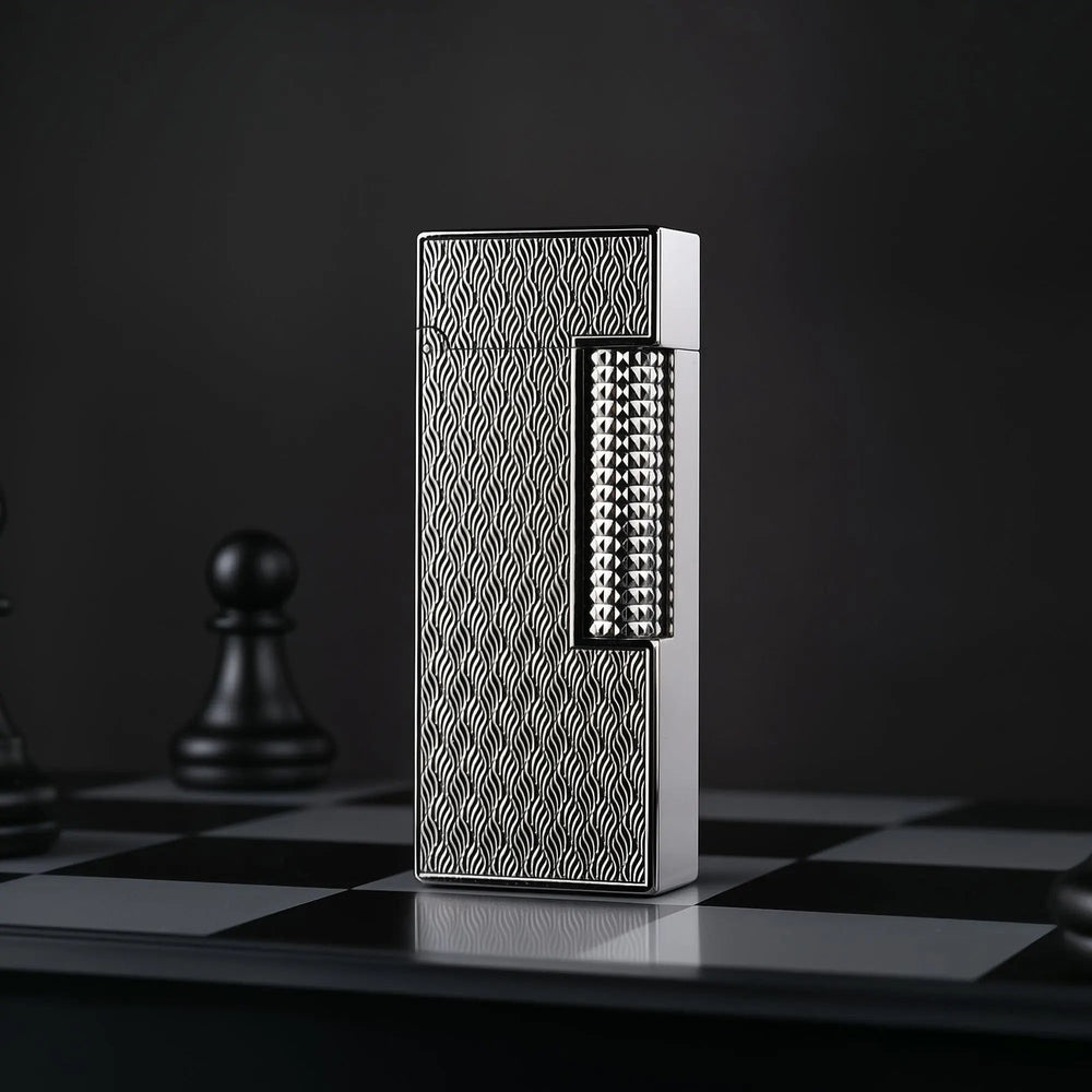 A vertical product shot of the Ripple Shadow narrow lighter standing on a chessboard. The silver-toned wavy texture of the lighter is in sharp focus, contrasted against a dark background with a blurred black chess pawn.
