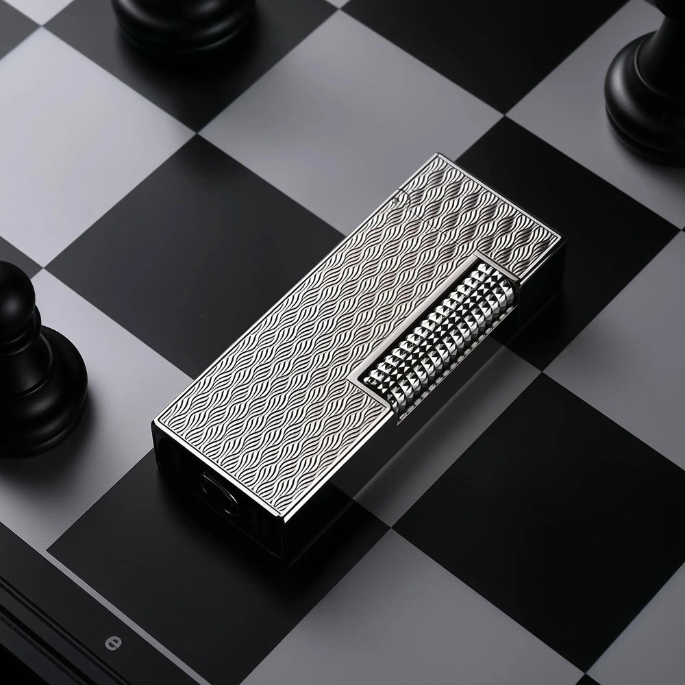 A Ripple Shadow narrow lighter lying diagonally on a black and grey chessboard, showcasing its silver-toned wavy "ripple" texture and polished hobnail ignition roller.