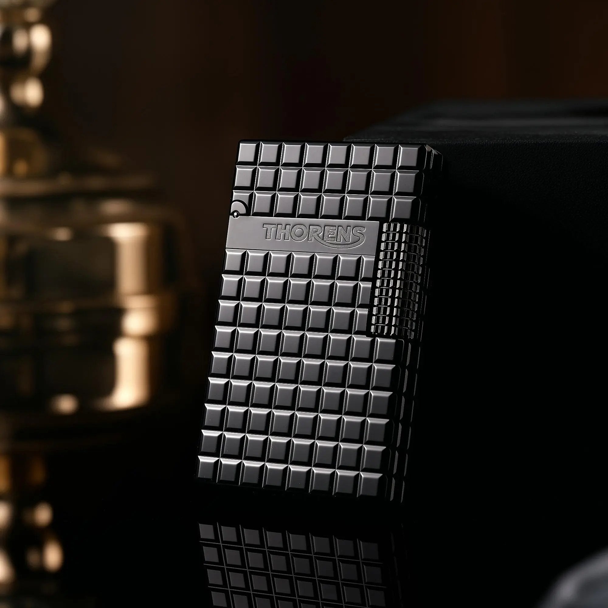 An onyx black Thorens side slip lighter leaning against a dark surface, highlighting the matte block pattern, side-roller ignition, and engraved logo.