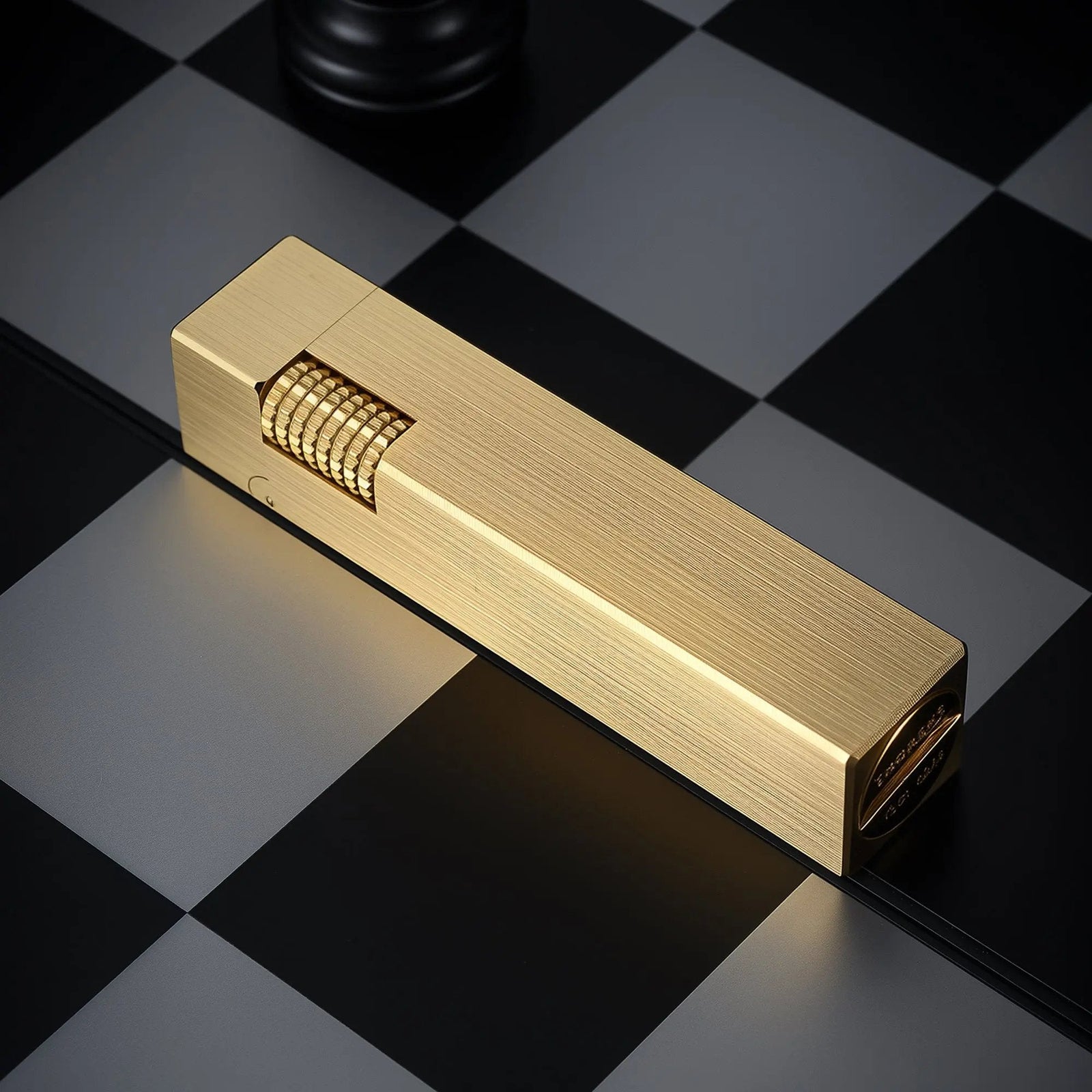 A glossy brass Side Slip rectangular lighter resting on a checkered surface, showcasing the mechanical flint wheel and refined metal texture.