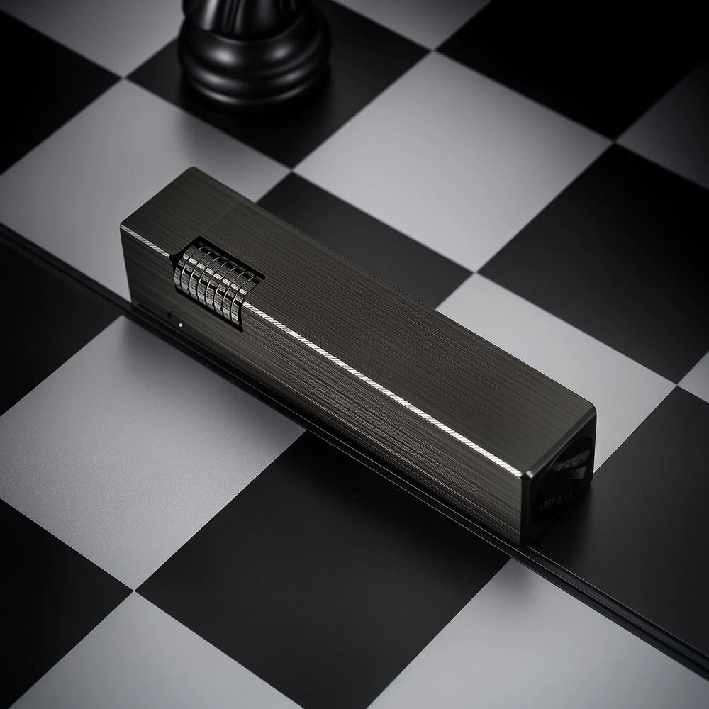 A Glossy Black Side Slip rectangular lighter with a refined brushed texture and silver-toned ignition roller, lying horizontally on a black and white checkered surface.