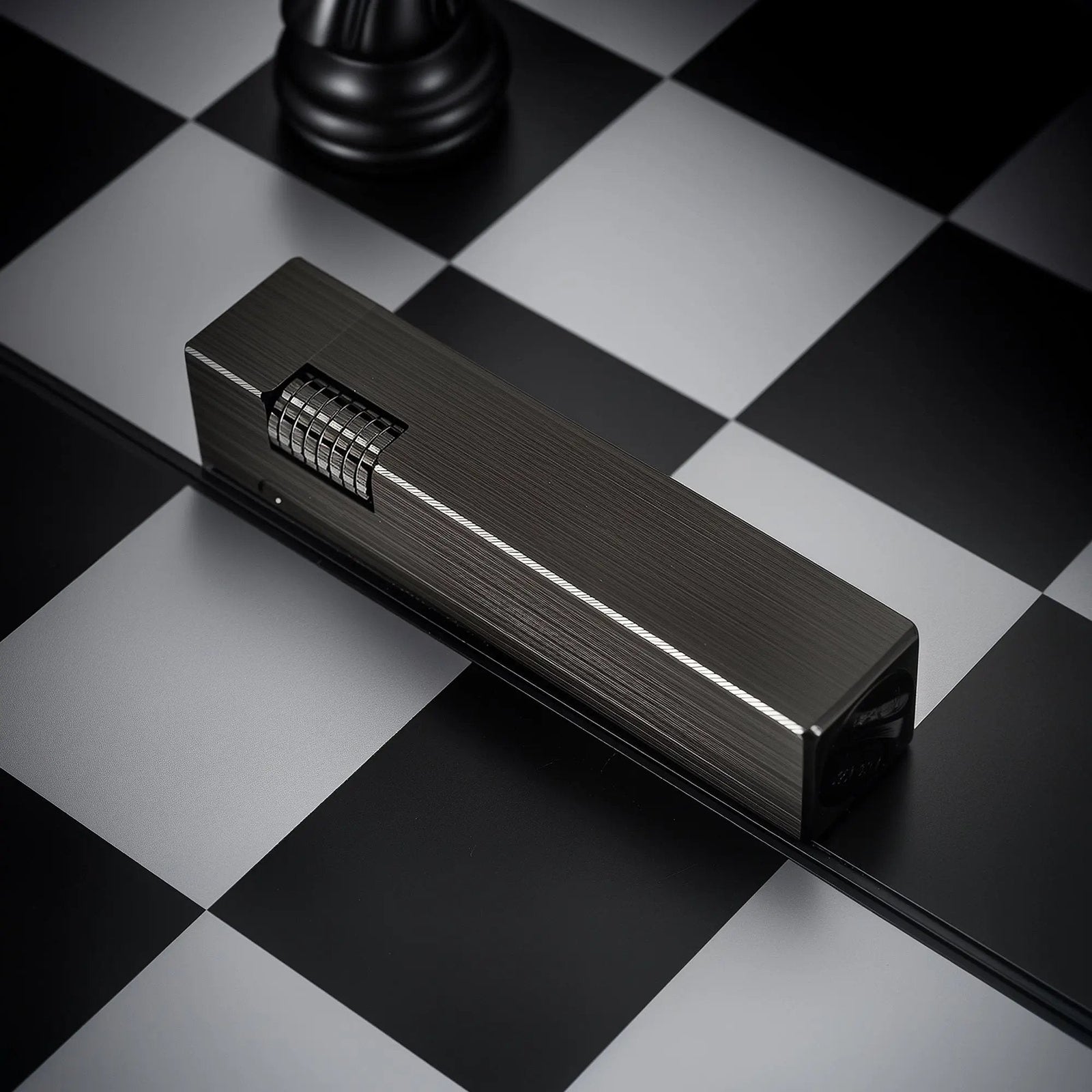 A Glossy Black Side Slip rectangular lighter with a refined brushed texture and silver-toned ignition roller, lying horizontally on a black and white checkered surface.