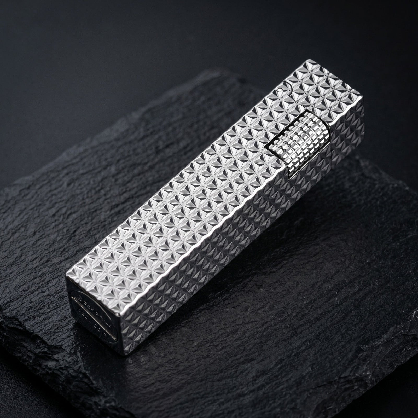 Thorens Side Slip rectangular lighter in silver starburst pattern shown closed on a dark textured surface, highlighting geometric engraving and ignition wheel.