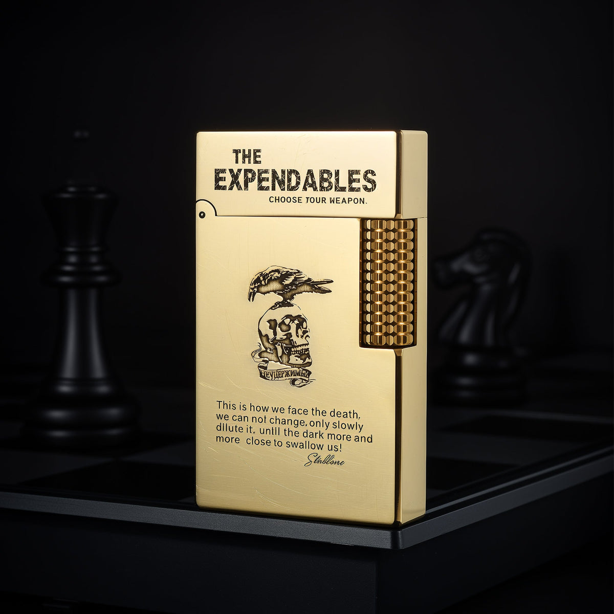 A gold Side Slip lighter featuring an etched skull emblem and The Expendables branding on a checkered background, showcasing its unique side-scrolling flint wheel.