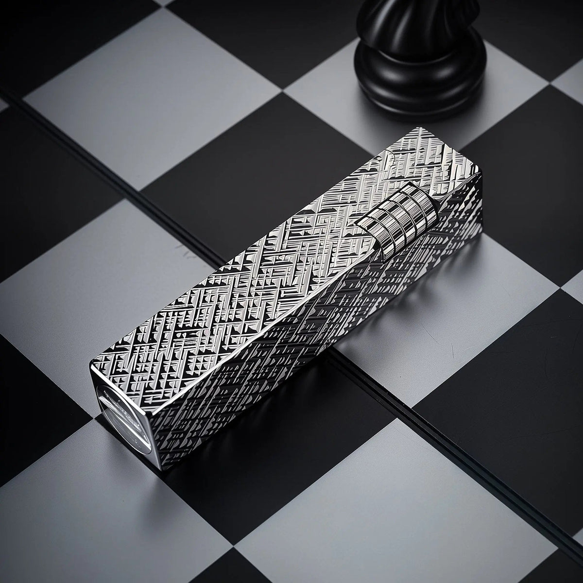 Silver carved Thorens rectangular side-slip lighter shown in an angled closed view, featuring an engraved geometric texture and exposed side ignition wheel on a black and white checkered