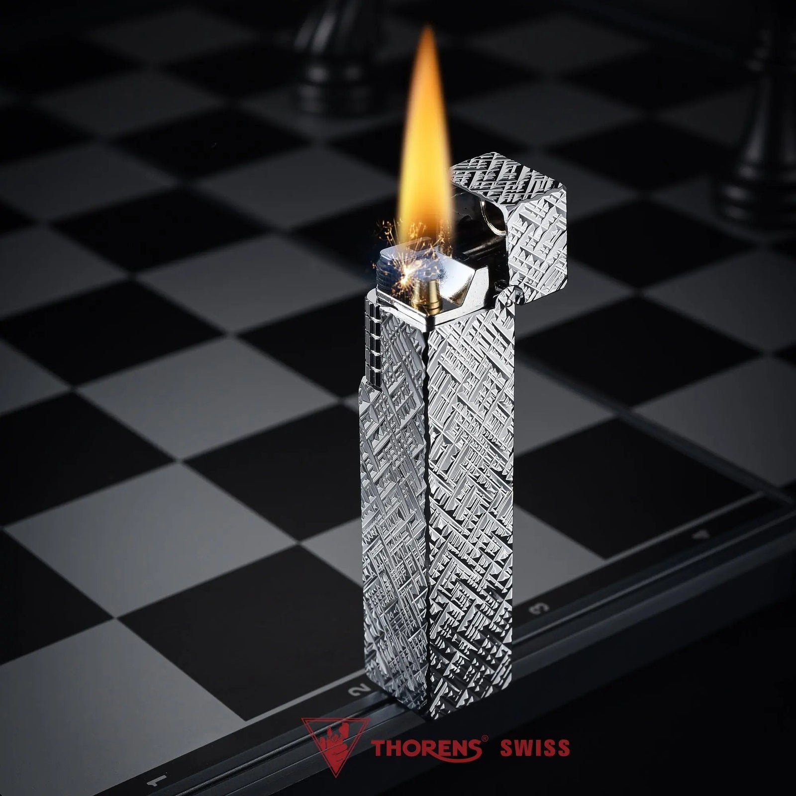 Silver carved Thorens rectangular side-slip lighter standing upright with the lid open and flame lit, featuring an engraved geometric texture, exposed ignition wheel, and visible wick on a black and white checkered surface