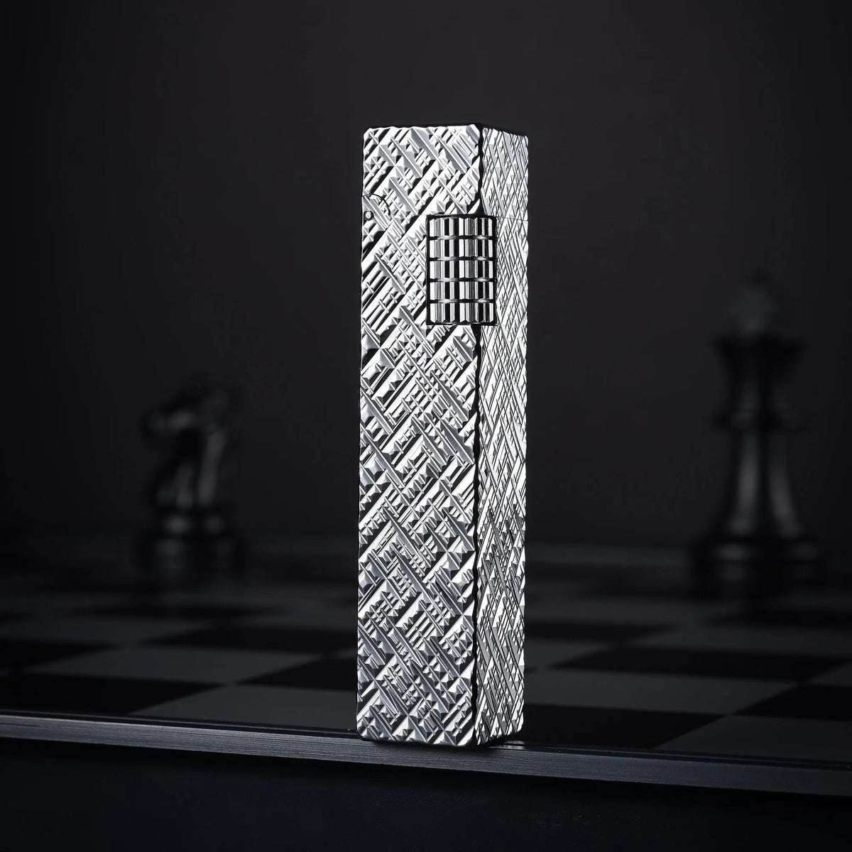 Silver carved Thorens rectangular side-slip lighter standing upright in the closed position, featuring an engraved geometric texture and exposed side ignition wheel against a dark checkered background
