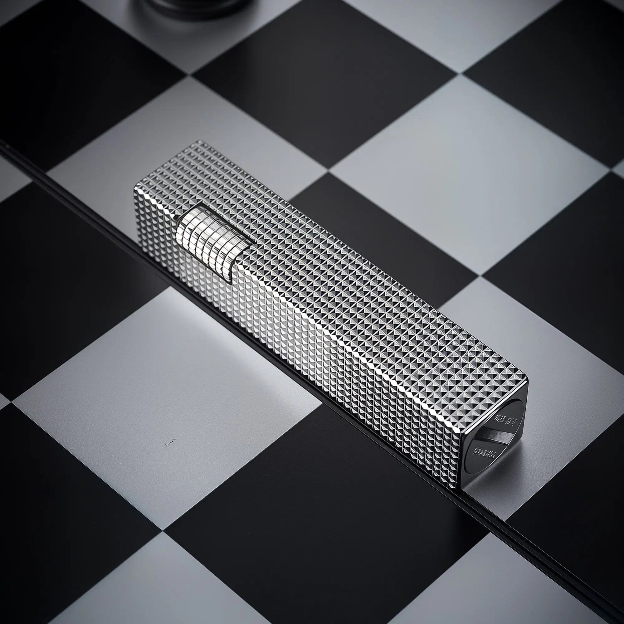 Angled view of a silver small square textured Thorens side-slip rectangular lighter on a black and white checkerboard surface