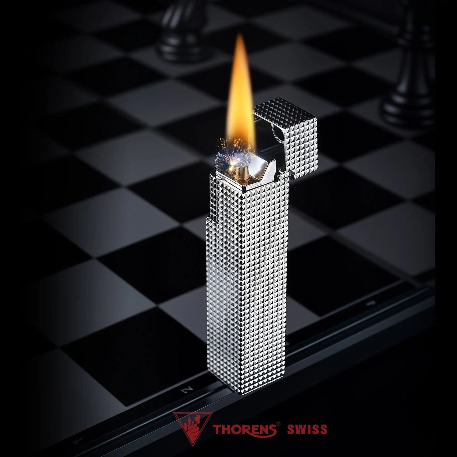 Lit silver small square textured Thorens side-slip rectangular lighter standing open on a black and white checkerboard surface