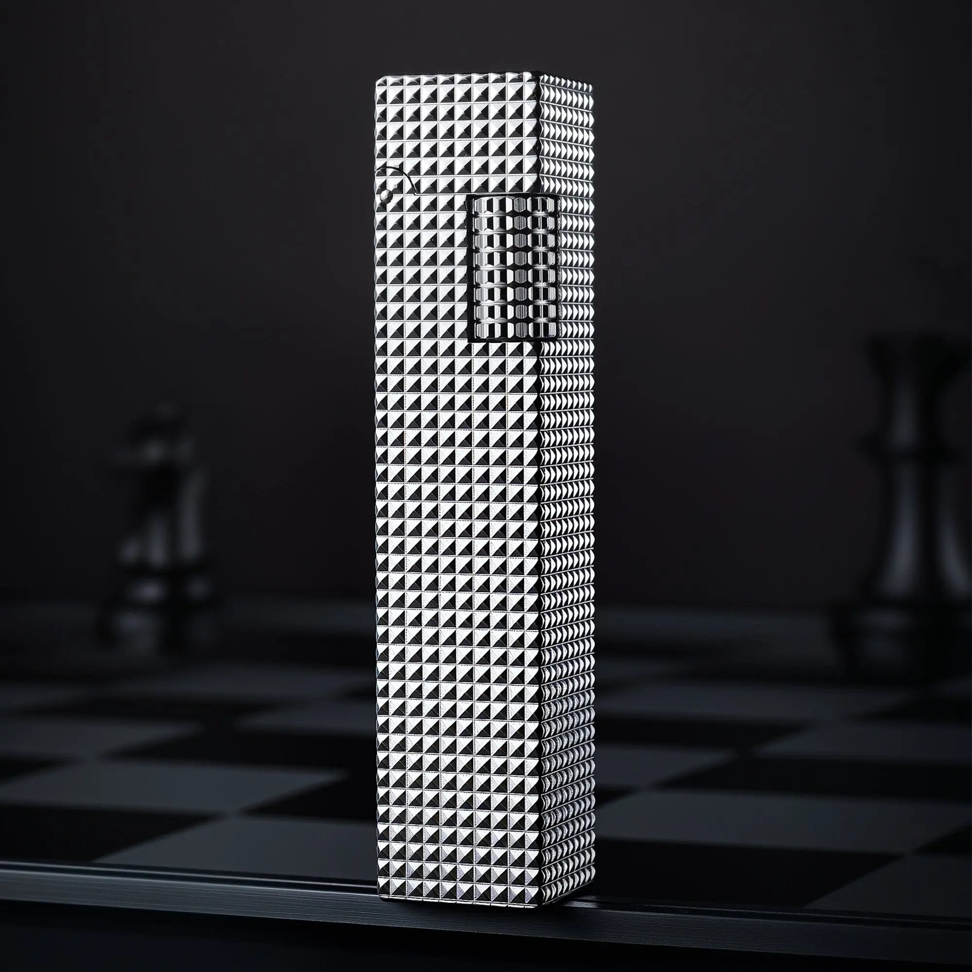 Silver small square textured Thorens side-slip rectangular lighter standing upright on a dark checkerboard surface