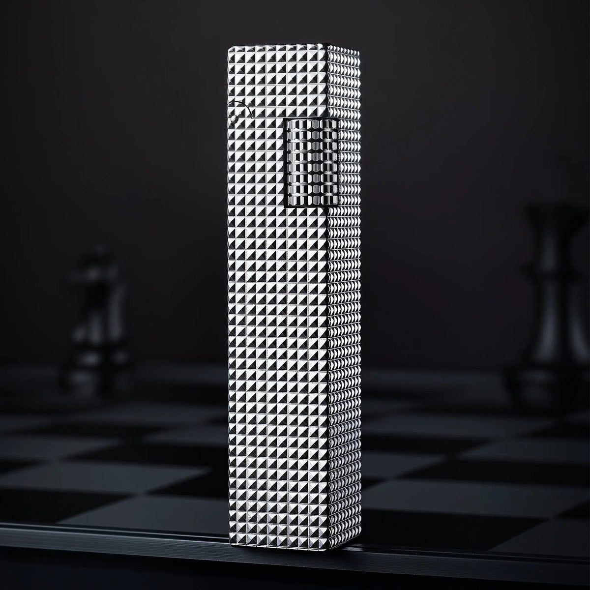 Silver small square textured Thorens side-slip rectangular lighter standing upright on a dark checkerboard surface