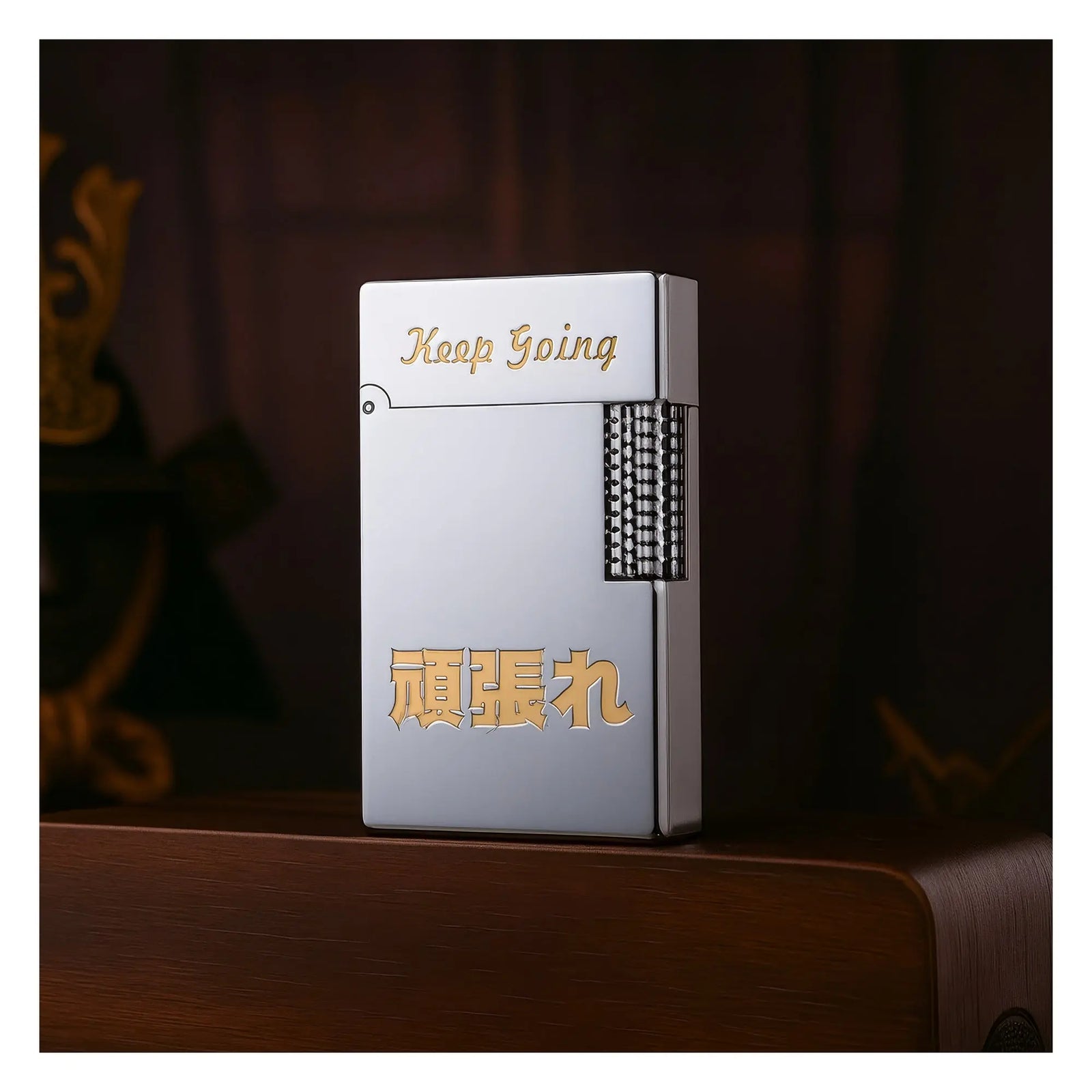 실버 톤의 Thorens 기계식 라이터. 골드 컬러의 "Keep Going" 문구와 일본어 상감 장식이 돋보이며, 나무 표면 위에 놓여 있어 정교한 황동 세공 기술과 수집 가치를 잘 보여줍니다.